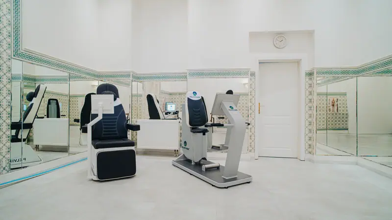 Therapiestuhl und Diagnosegerät des Systems PelviPower in einem hellen Behandlungsraum mit Spiegelwänden im Hotel Nové Lázně