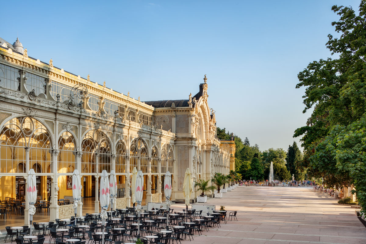 Die Hauptkolonnade von Marienbad mit Café-Tischen unter der Gusseisenkonstruktion und der Promenade dahinter