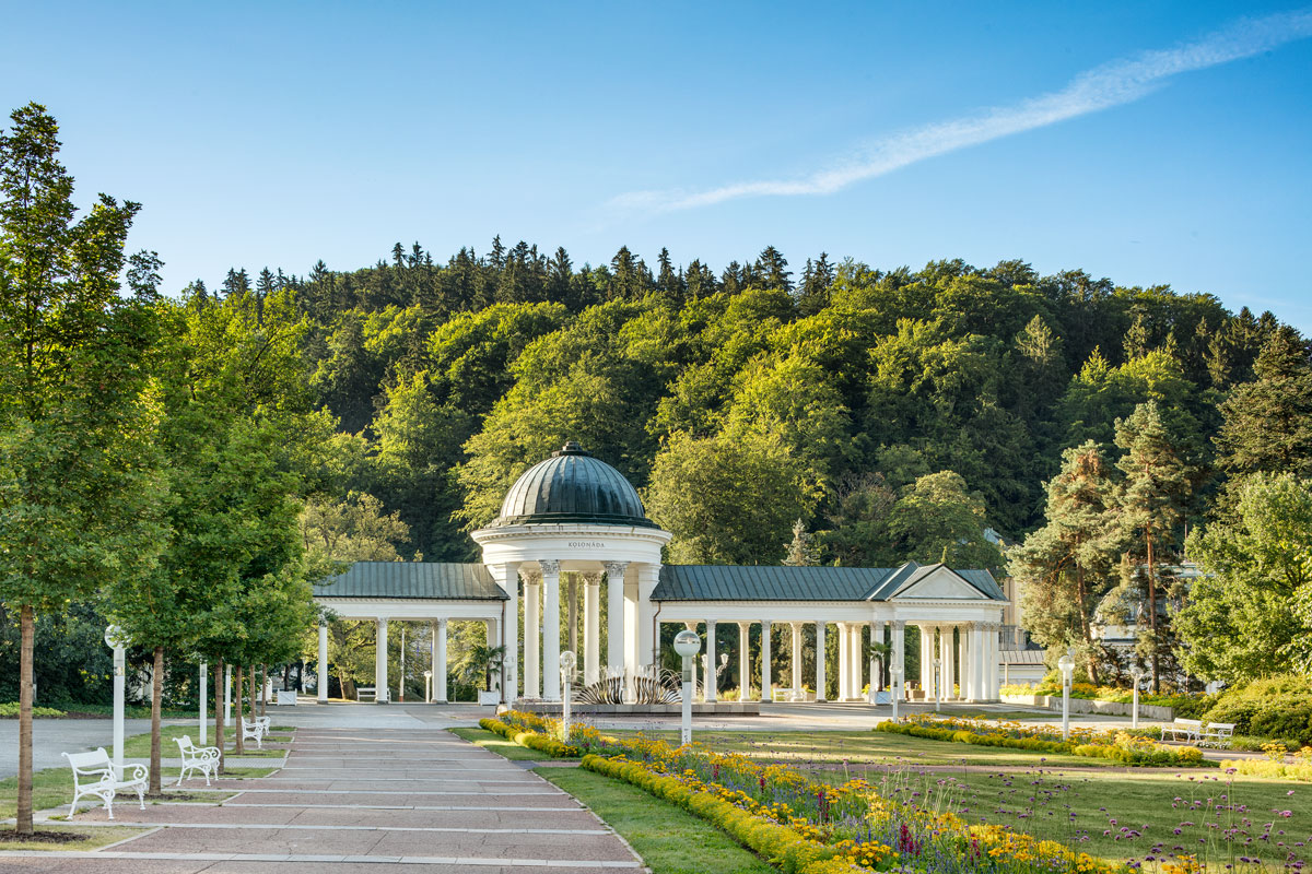 White columned pavilion of the Rudolf and Caroline springs in the spa park, with a wooded hillside behind