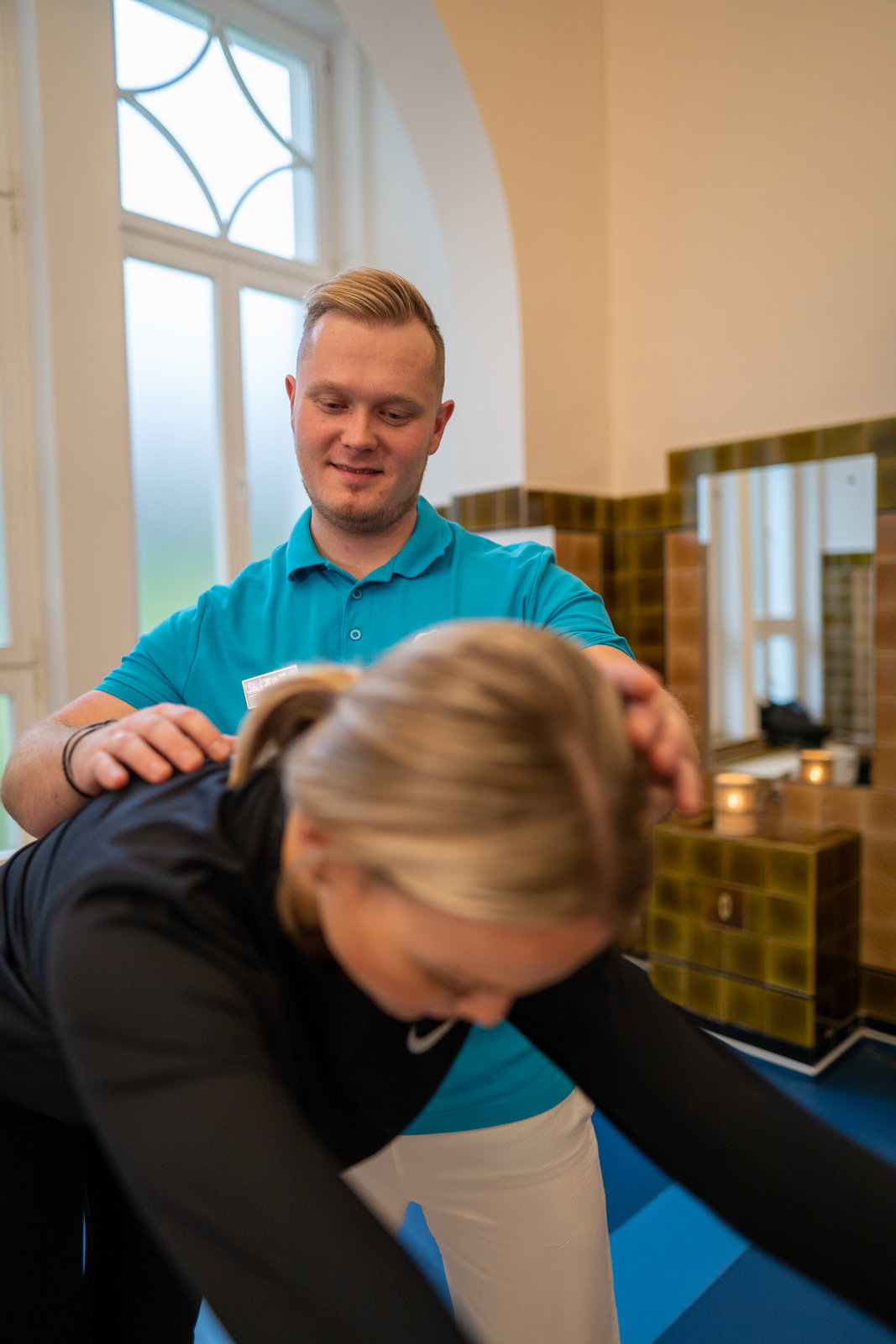 Der leitende Physiotherapeut der Léčebné lázně Mariánské Lázně – Ensana zeigt physiotherapeutische Übungen: Er leitet eine Gästin bei einer seitlichen Dehnung an.