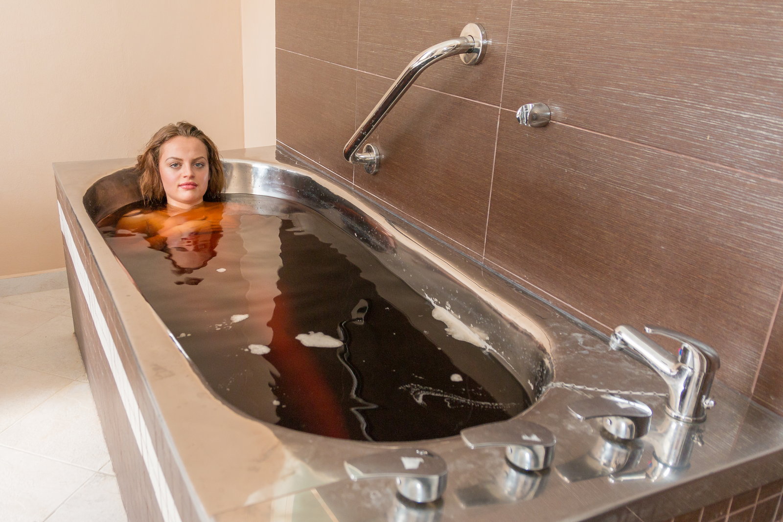 Eine Frau ruht mit ruhigem Gesichtsausdruck in einem dunklen Mineralbad, das Wasser reicht ihr bis zu den Schultern