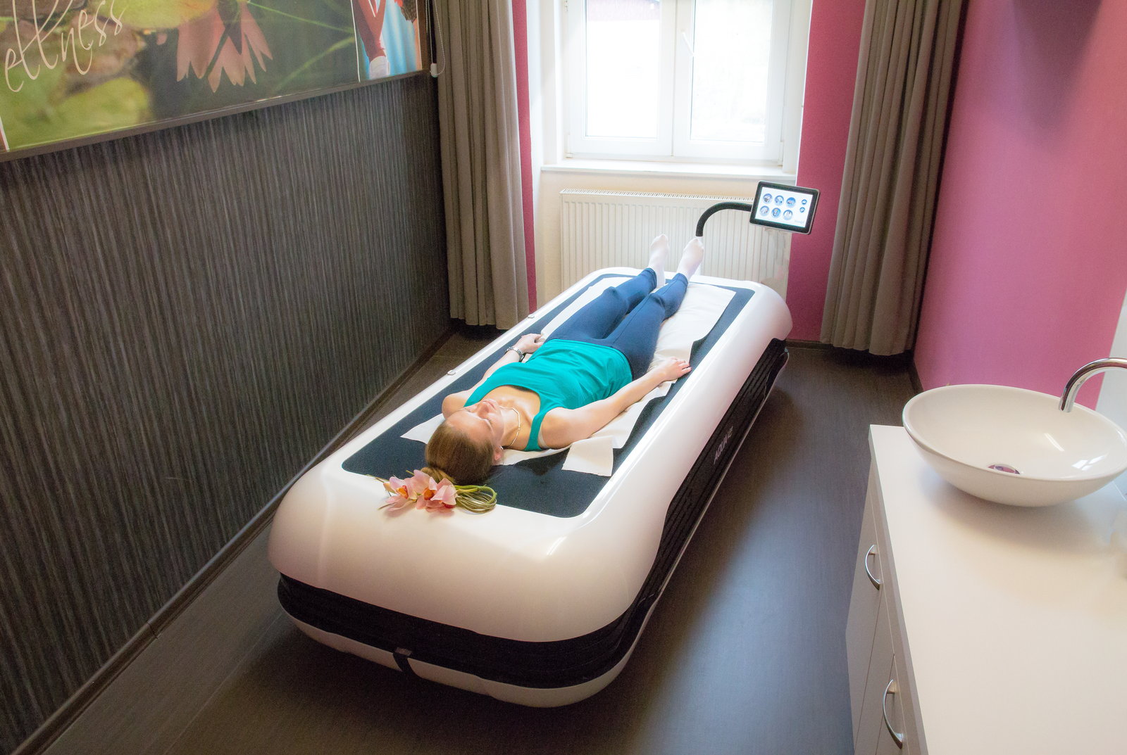 Eine Gästin liegt bekleidet auf einer Liege für die trockene Wassermassage, daneben das Bedienfeld